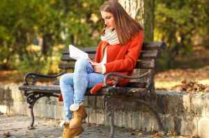 Young girl sitting on a park bench and reading a book, on a beau